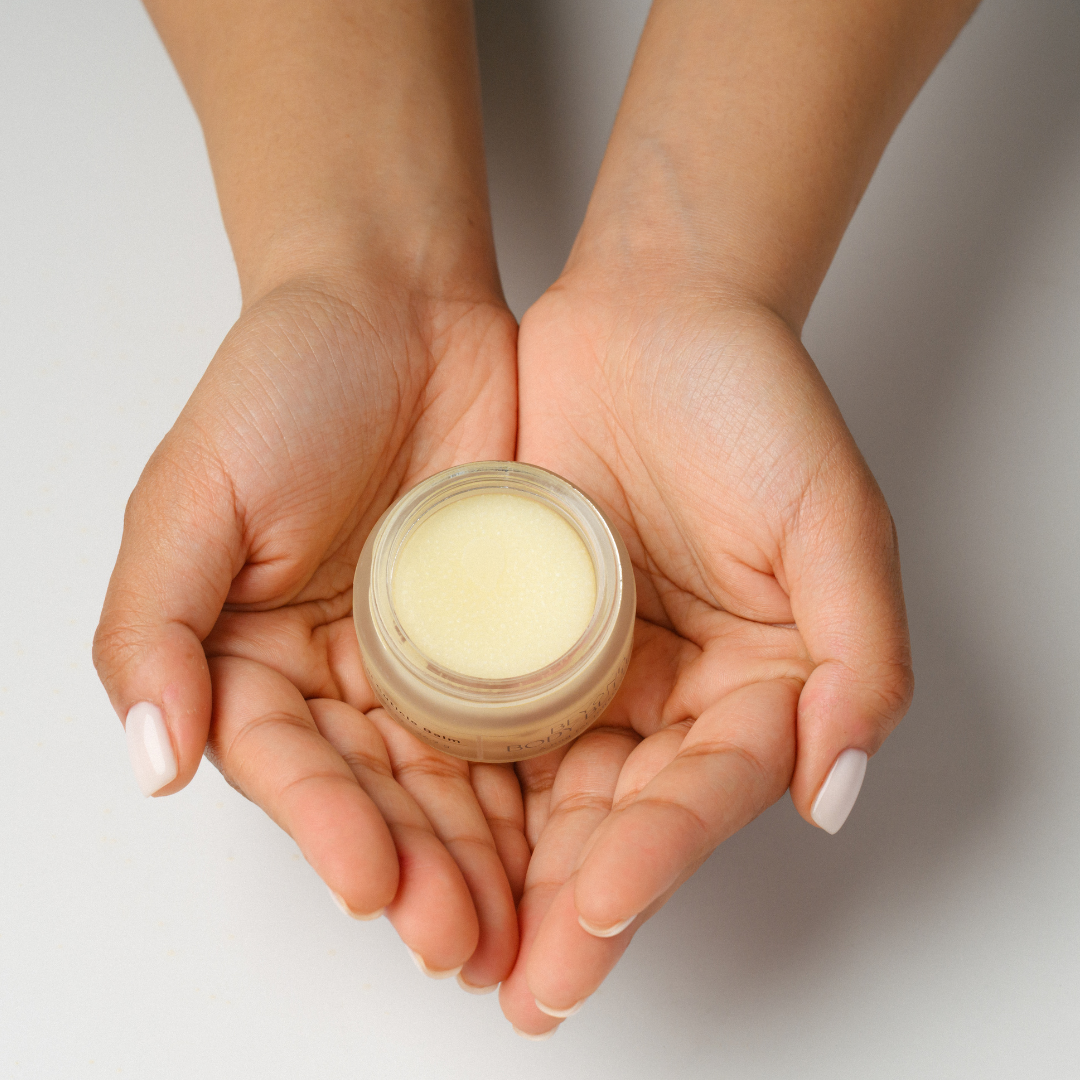 Two hands holding a small jar of cream against a neutral background