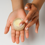 Person holding a small jar of cream in one hand with a neutral background